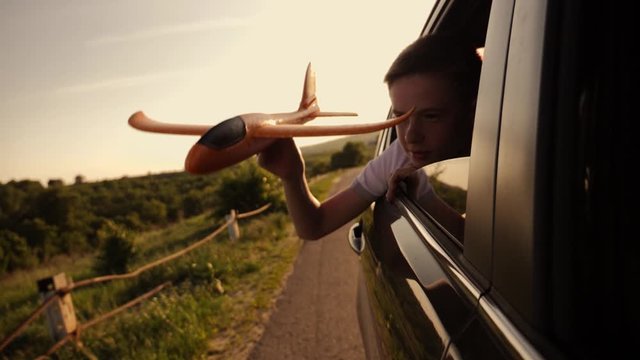 A boy with an airplane model in his hands plays traveling by car. Fantasy baby in the sun at sunset. Striving for victory and success. The concept of lifestyle and the path to success.