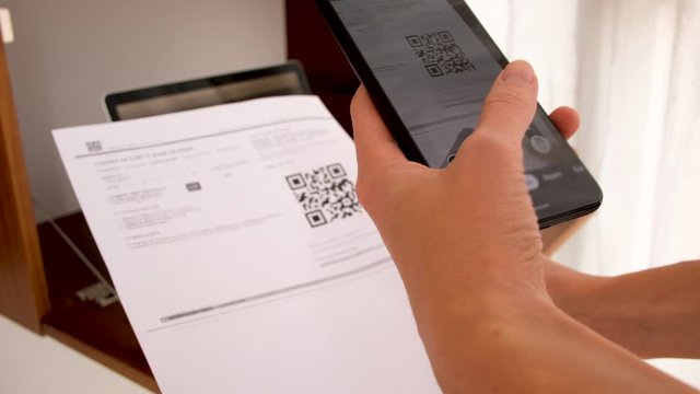 Hand with phone scans QR Code on background of a laptop with a workplace