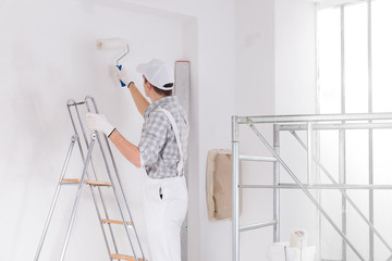 Painter standing on a ladder painting a white wall - 339112363