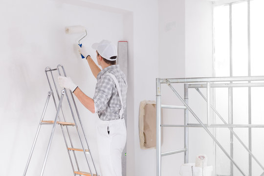 Painter standing on a ladder painting a white wall