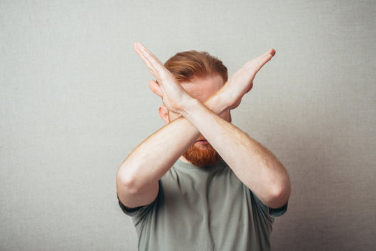 Serious and determined Young hipster red bearded Man makes an X shape with his arms and hands. stop, cross, or