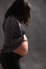 Pregnant woman standing in profile hugging her belly