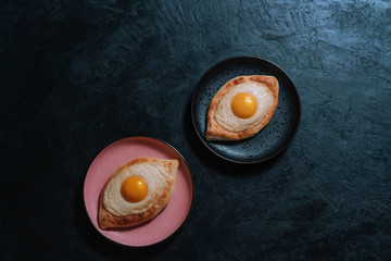 Two Adjarian khachapuri on a pink and black plate on a dark background.