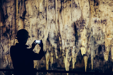 Obraz na płótnie Canvas Silhouette of a man taking pictures in a cave with smartphone.