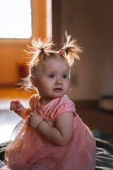 Cute baby in a pink dress with two ponytails in her hands for self-isolation .