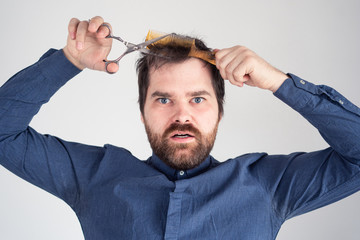 Obraz premium man with a comb and scissors in his hands cuts his hair