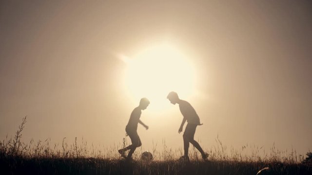 Two boys playing football at sunset. Silhouette of children playing with a ball at sunset. The concept of a happy family and a healthy lifestyle