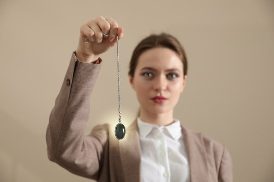 Psychotherapist with pendulum on beige background. Hypnotherapy session