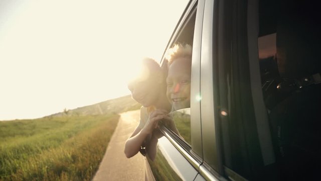 Happy family traveling by car. Two boys in the car window waving their hands in the sun at sunset.