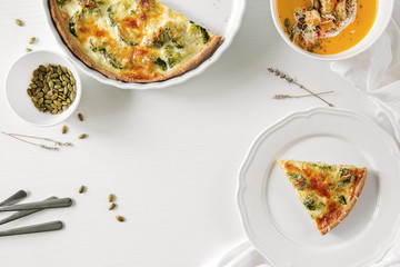 Pie with broccoli, pumpkin pumpkin bite, seeds and crackers lie on a white table. Nearby is a white towel and serving utensils.