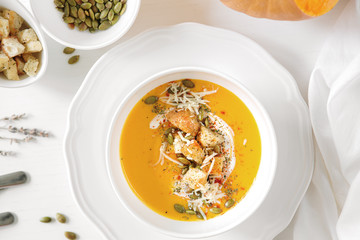 Pumpkin soup, a piece of pumpkin, seeds and crackers lie on a white table. Nearby is a white towel and serving utensils. Close up.