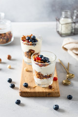 Morning granola breakfast with raisins, cranberries and hazelnuts served with yogurt in glasses on a white concrete background. Side view, copy space. Menu, recipe