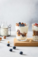 Healthy breakfast granola, muesli with blueberries, nuts, honey and yogurt in glasses on gray concrete background. Copy space, side view