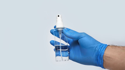 A male hand in a blue medical glove holds an antiseptic against coronavirus . Isolated on a gray background in the studio. Coronavirus concept.