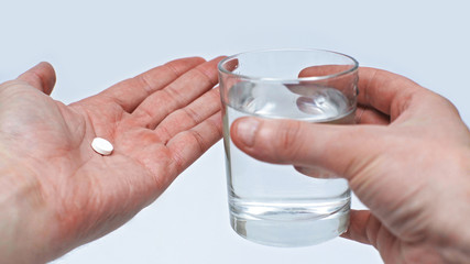 The male hand holds a glass of clean water to drink medicine to protect against coronavirus during quarantine. Isolated on a gray background in the studio. Coronavirus concept