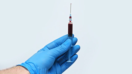 A male hand in a blue medical glove holds an injection syringe against coronavirus. Isolated on a gray background in the studio. Coronavirus concept.