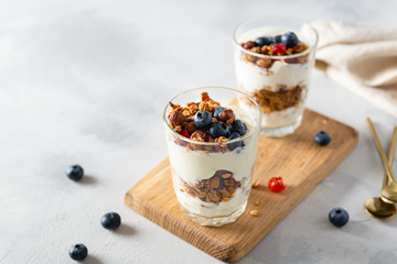 Parfait. Glasses with homemade granola with yogurt and fresh berries on white concrete background. Dieting, recipe. Side view, copy space