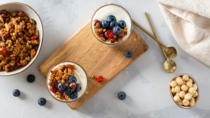 Morning granola breakfast with raisins, cranberries and hazelnuts served with yogurt in glasses on a white concrete background. Top view. Menu, recipe