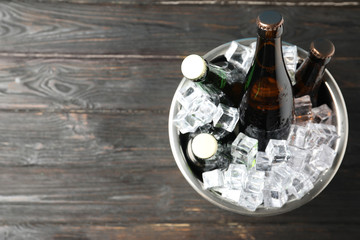 Metal bucket with bottles of beer and ice cubes on black wooden background, top view. Space for text