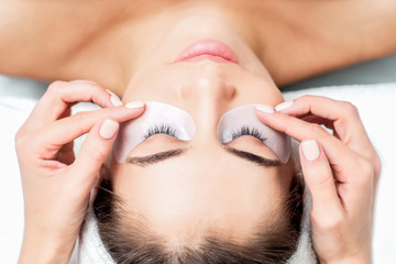 Cosmetologist hands glueing duct tape under eyes of young woman before eyelash extension procedure, top view.