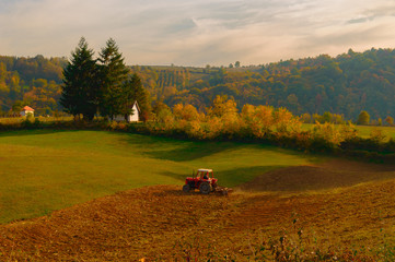 Obraz premium Seasonal work on farm. Plowing land in autumn. Red tractor in field. Agro bussines .