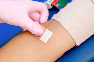 Nurse hand is glueing an adhesive plaster on arm wearing rubber protective gloves after blood...