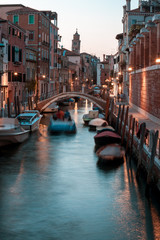 Fototapeta na wymiar Narrow canal with boats and vintage houses at dusk. Venice city at night