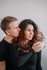 Minimalistic portrait of a blond man and a girl with long hair, both dressed in black, they are embracing