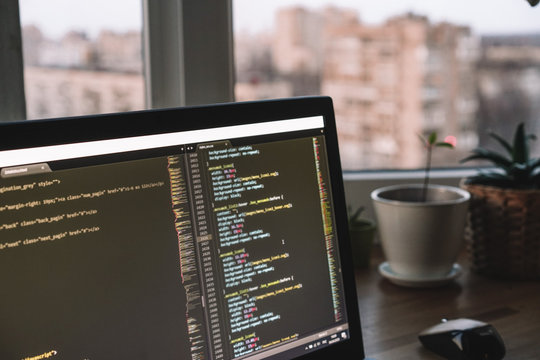 A laptop with an open program and code is on the windowsill