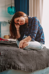 Fototapeta premium A brunette girl with long hair in a checked shirt is lying on the bed in a beautiful modern bright cozy interior
