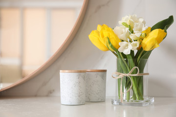 Beautiful yellow tulips and freesia flowers near mirror on white table, space for text