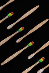 Group of white and rainbow eco bamboo toothbrushes, on black background. Top view. Natural organic product for oral hygiene. Dental zero waste and no plastic concept. Safe for the earth.