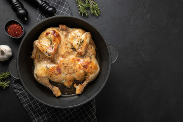 Roasted chicken with spices in cast iron pan on black table. Space for text or recipe. View from...