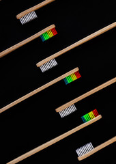 Group of white and rainbow eco bamboo toothbrushes, on black background. Top view. Natural organic product for oral hygiene. Dental zero waste and no plastic concept. Safe for the earth.