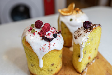 Various Easter cakes with white icing, decorated with berries and orange stand on a wooden board. Easter cutaway