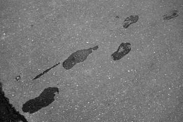 Wet foot steps on asphalt in black and white.