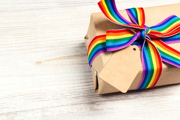 Gift box with rainbow LGBT ribbon and empty tag for inscription on a light wooden background....