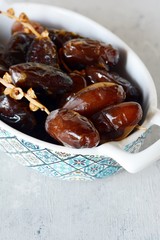 Bowl with juicy dates on a branch on a gray-blue background. Healthy tasty food. Raw Organic Medjool Dates 