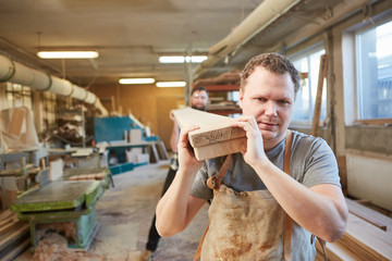 Carpenter apprentice and a colleague carry beams