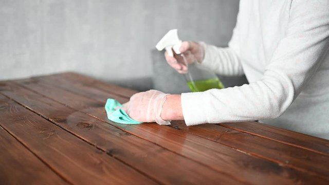 Close up of cleaning home wood table, sanitizing kitchen table surface with disinfectant antibacterial spray bottle, washing surfaces with towel and gloves. COVID-19 prevention sanitizing inside.