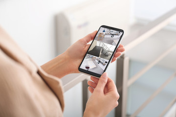 Woman monitoring modern cctv cameras on smartphone indoors, closeup. Home security system