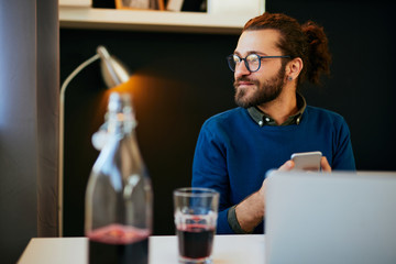 Attractive Caucasian bearded entrepreneur sitting in his office, using smart phone and taking a break from work.