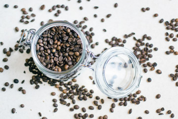 Macro shot of a transparent jar filled with coffee beans in the center of the photo and coffee beans around the jar