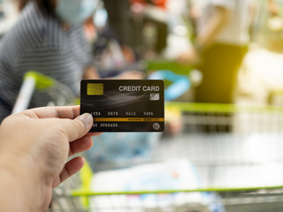 Hand holding Credit card on supermarket. Use credit card to pay for food and Cashier counter blurred background.Shopping concept.