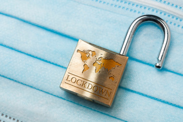 Coronavirus world lockdown end: a lock with a world map and the word lockdown engraved on a light blue surgical mask.