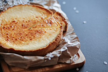 Tasty homemade cheesecake on wooden board and black table with blooming branch.