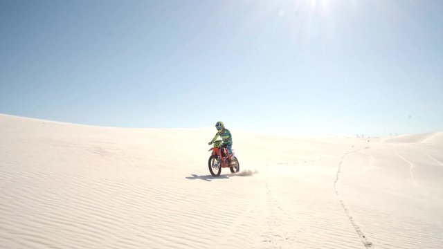 Motocross racer riding over sand in desert. Motocross biker driving bike fast over sand dunes.
