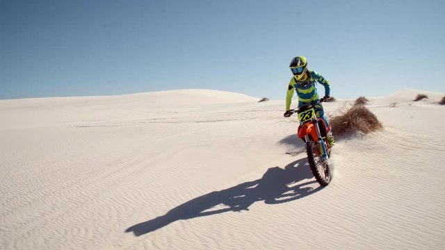 Professional male dirt biker practising his skill in desert. Motocross bike racer off roading on sand dunes.
