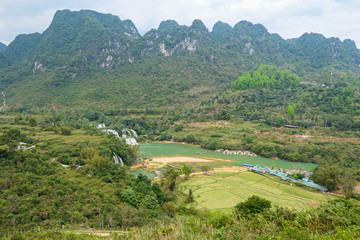 Full of water huge waterfall near the green forest with green trees in mountains from the top view.