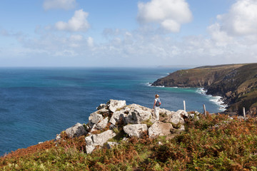 Woman standing on a rocky clifftop looking at the stunning coastal scenery near St Ives in...